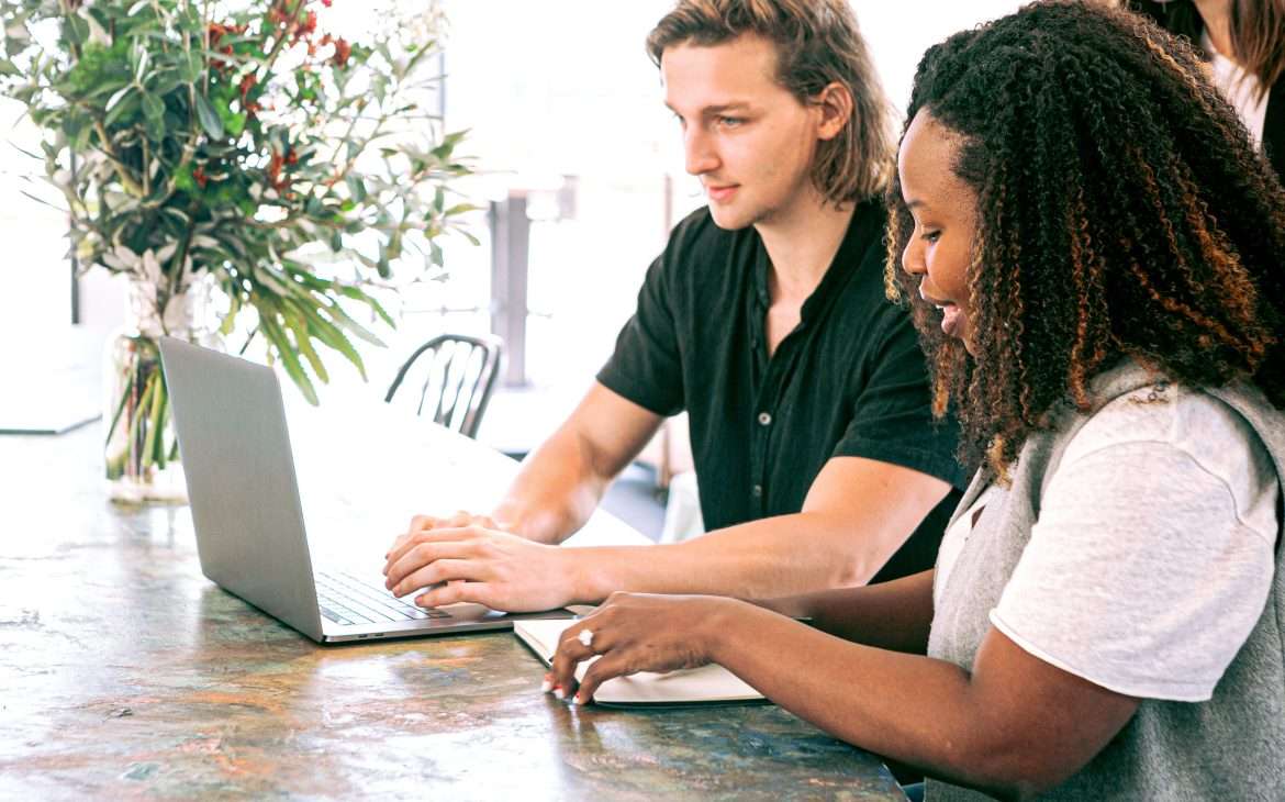 a man working on a laptop while a woman takes notes